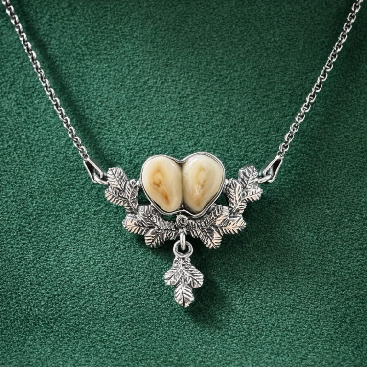 A hunting-inspired necklace made from a pair of doe grandles set in silver and framed by spruce branches
